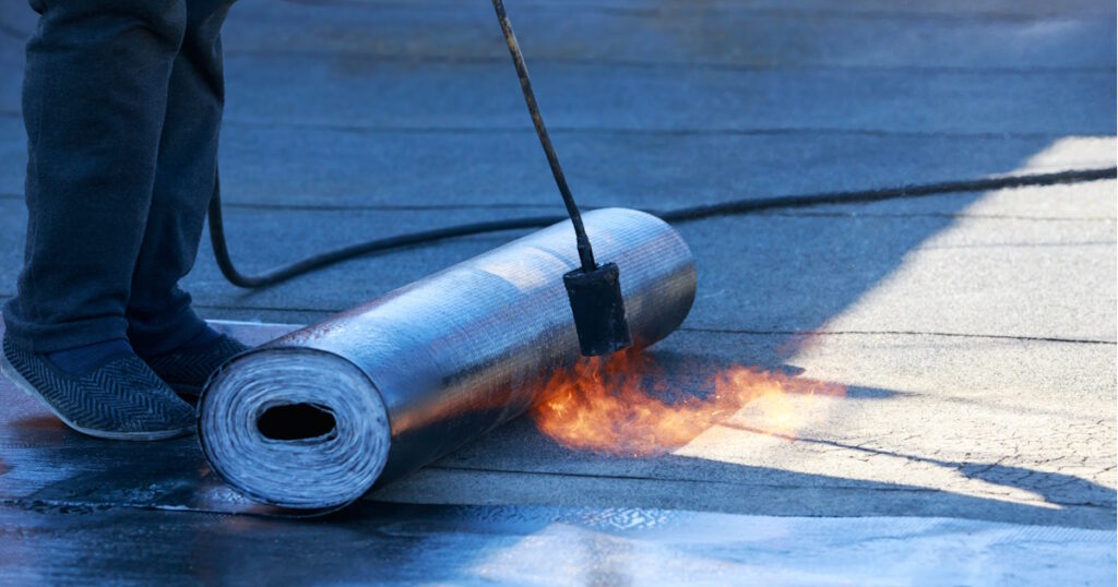 Een dakdekker brengt een laag dakbdekking aan met een brander.
