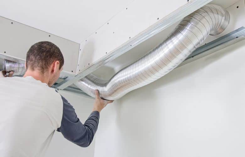 Een monteur legt een ventilatiesysteem aan. Door een vochtige ruimte goed te ventileren wordt de ruimte weer droog.