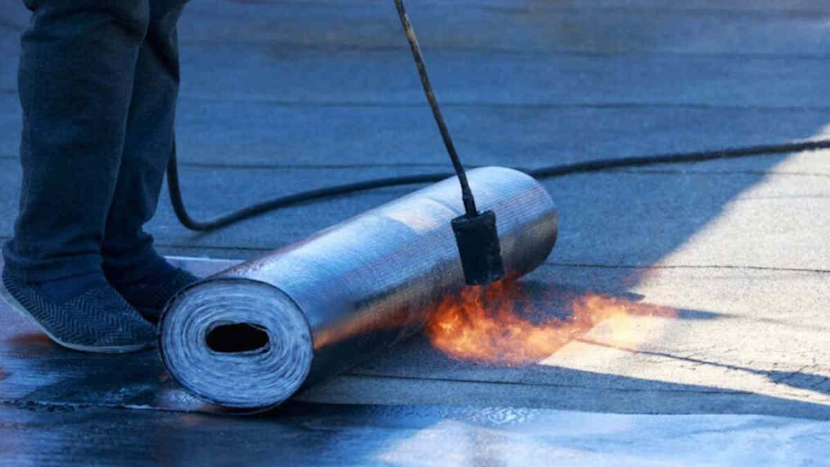 Een dakdekker brengt een laag dakbdekking aan met een brander.